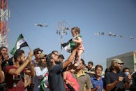 在叙利亚伊德利卜，一群热情洋溢的人们在户外欢庆，旗帜飘扬，场面充满希望与团结