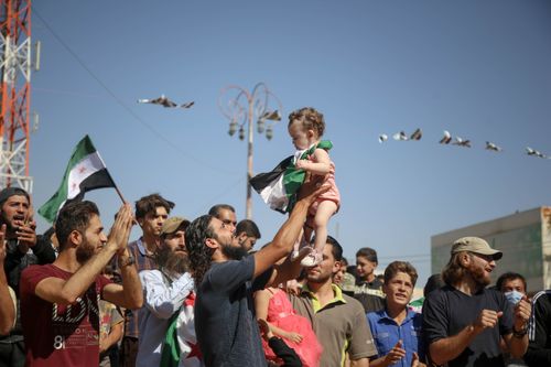 Free A spirited crowd celebrates outdoors in Idlib, Syria, symbolizing hope and unity. Flags wave amid the joyful scene. Stock Photo