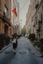 Woman in Black Dress Walking on Street between Old Buildings