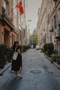 Woman in Black Dress Walking on Street between Old Buildings