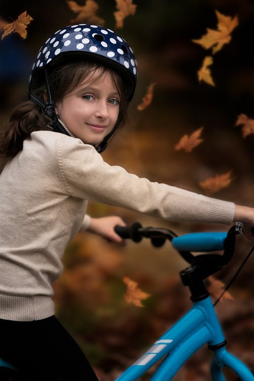 Content girl in helmet and sweater riding bicycle in autumn park and looking at camera