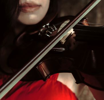 Crop unrecognizable lady in red clothes playing music on violin in light place