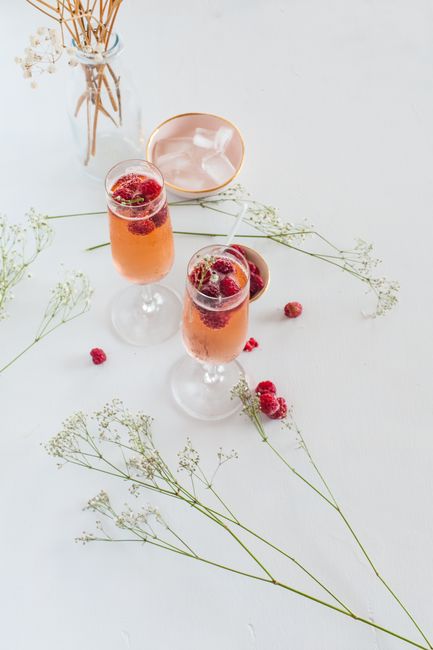 A refreshing raspberry mocktail served in wine glasses with decorative flowers in a bright setting.