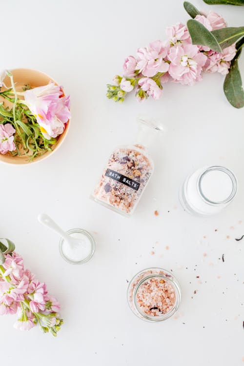 Free Top view of fresh delicate Brompton stock flowers with pink petals placed on white table with various jars of bath salts Stock Photo