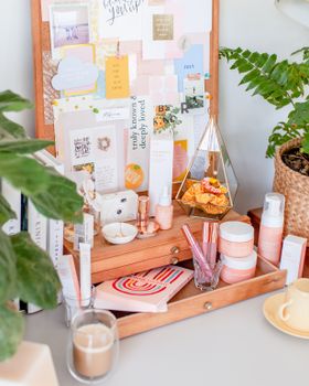 Stylish wooden box with assorted cosmetic and beauty products placed on white dressing table near fresh potted plants and candles
