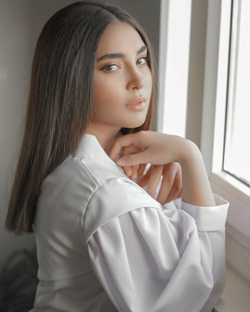 Woman in White Blouse Leaning Beside a Window