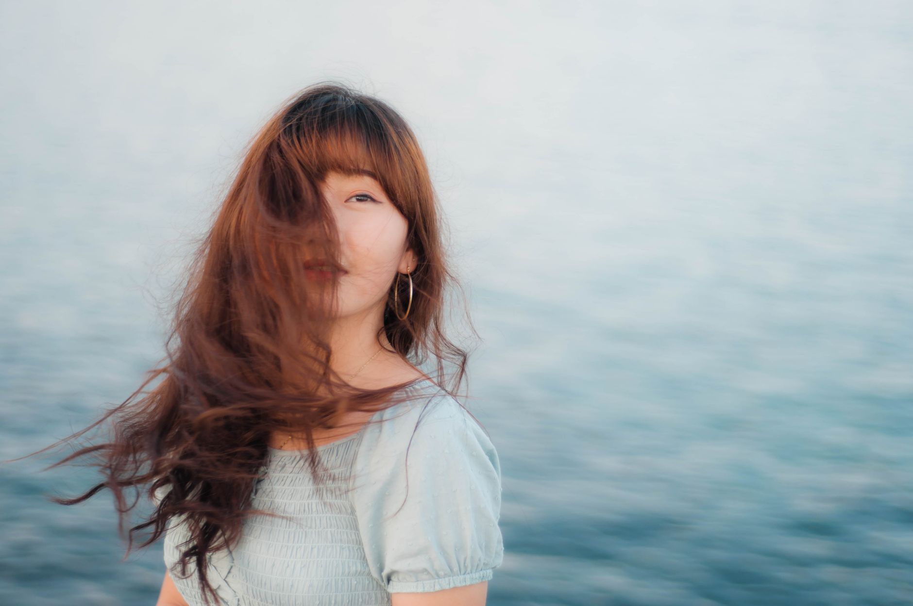 Portrait of a young woman with long hair covering her face, standing by the sea.