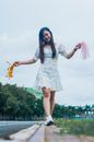 Cheerful Asian woman walking on roadside with streamer pom poms