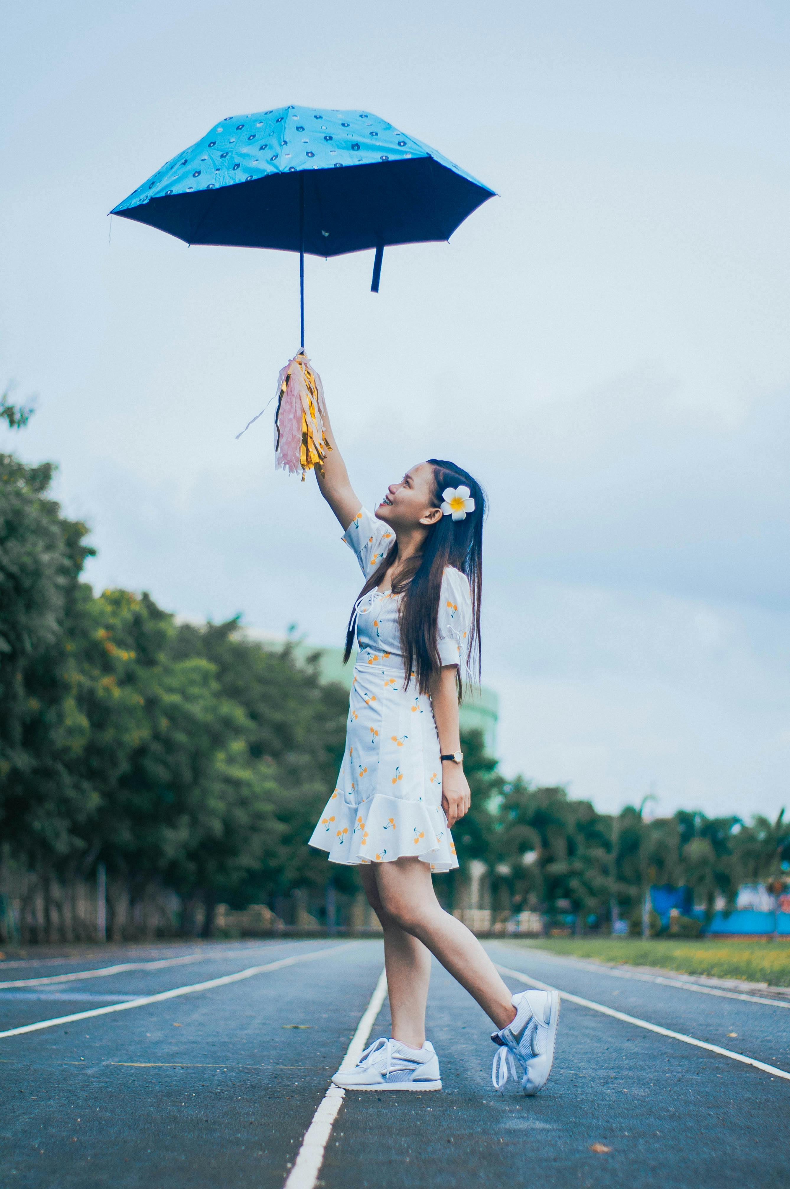 一名穿着正装的少数民族女性侧身站在跑道上，撑着雨伞和绒球