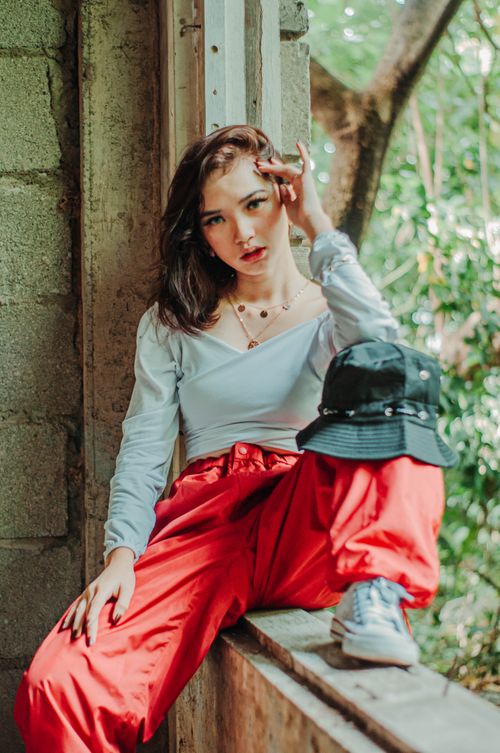 Free Self confident female millennial wearing fashionable outfit sitting on wooden window frame of old building and looking at camera Stock Photo