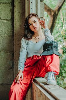 Self confident young female in stylish outfit sitting in old abandoned building and looking at camera
