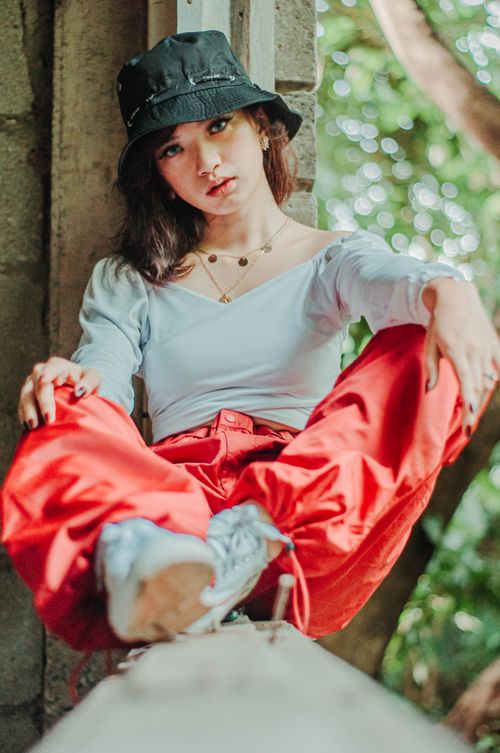 Free Full body of serious young female wearing hat and modern stylish outfit sitting confidently in shabby destroyed building and looking at camera Stock Photo