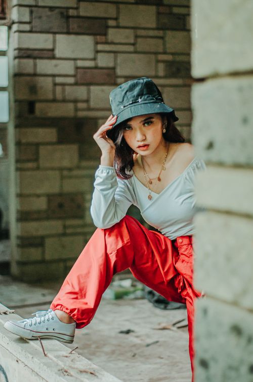 Free Asian female with hat in abandoned building looking at camera and putting foot on window opening Stock Photo