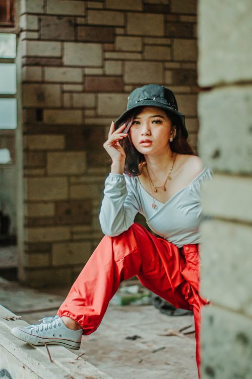 Free Serious Asian female in green hat looking at camera in old building with foot on window opening against blurred background Stock Photo