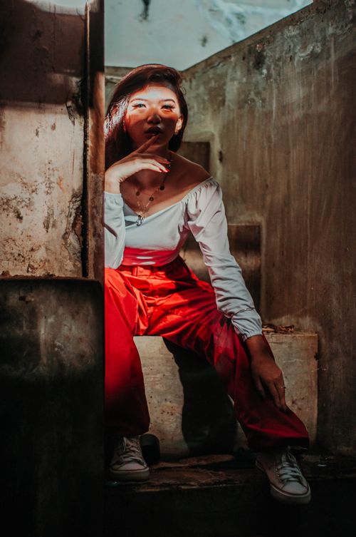 Free Asian woman sitting in abandoned building while looking at camera with hand at chin Stock Photo