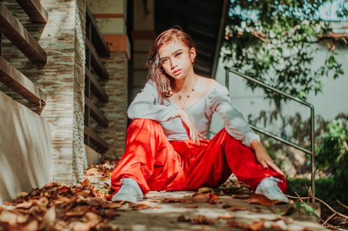 Free Ethnic female with spread legs sitting on wooden stairs with fallen foliage while looking at camera Stock Photo