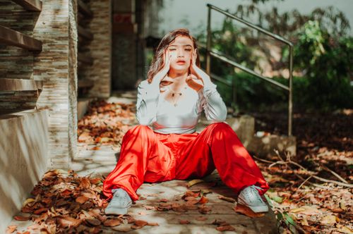 Free Asian woman in red pants closing eyes on wooden stairs and holding head on blurred background Stock Photo