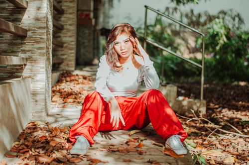 Free Self confident ethnic female teenager in stylish outfit looking at camera while sitting on footpath in fall Stock Photo