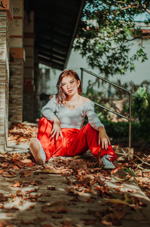 Free Self confident Asian female adolescent looking at camera while sitting on dry leaves in sunlight Stock Photo