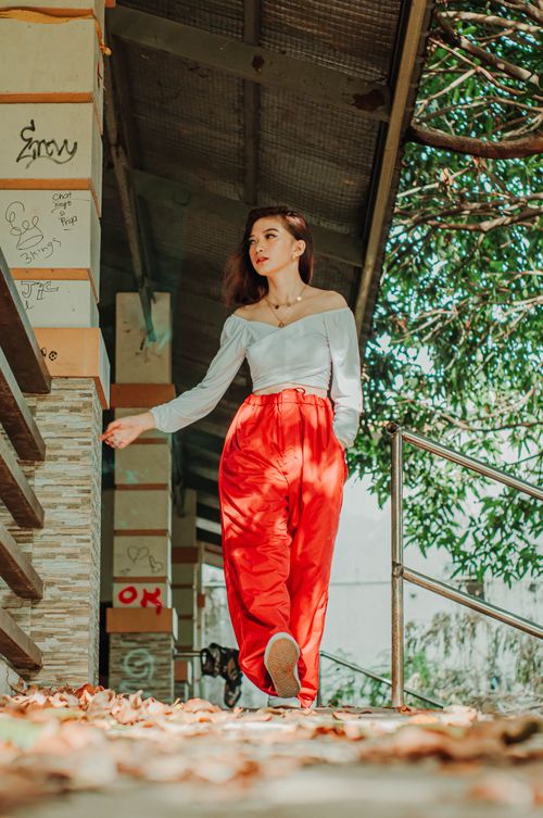 Free Ground level of stylish Asian female teenager with hand in pocket touching building wall while strolling on walkway and looking away Stock Photo