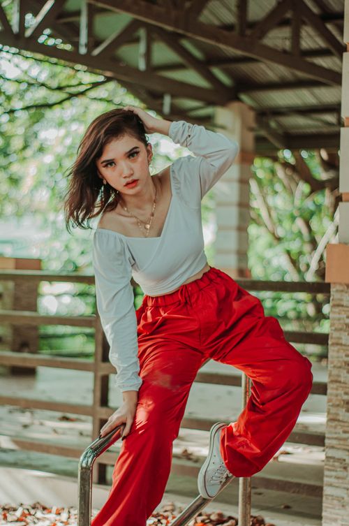 Free Serious cool female in trendy outfit looking at camera while sitting on metal railing near fence on terrace under roof Stock Photo