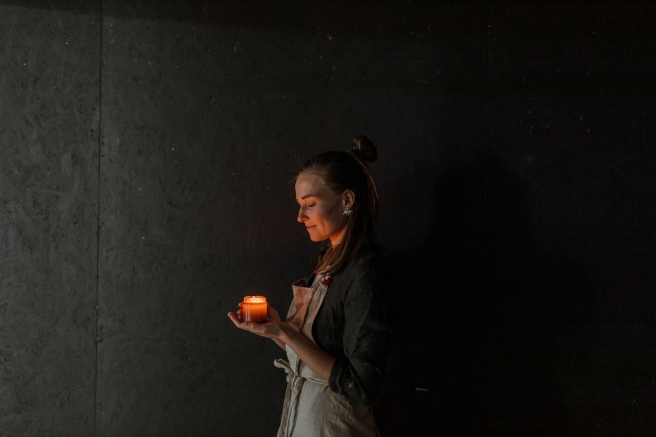 A woman in an apron holds a lit candle in a dimly lit room, creating a serene ambiance.