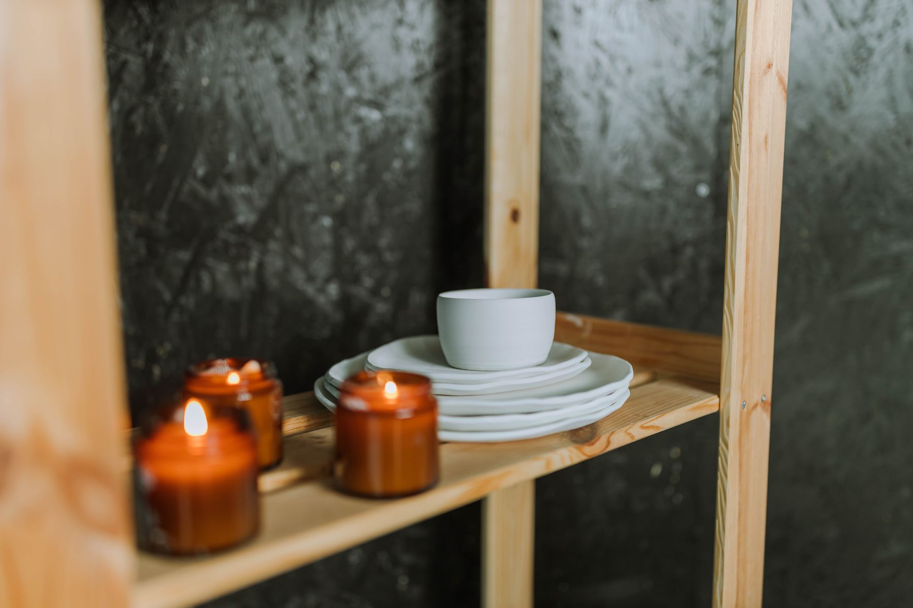 Amber candle jars and stacked ceramics on a pale wooden shelf — Anastasia Shuraeva on Pexels
