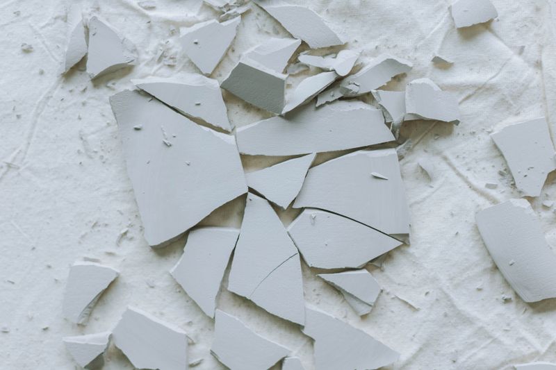 Broken ceramic tiles scattered on a textured white surface, creating an abstract composition.