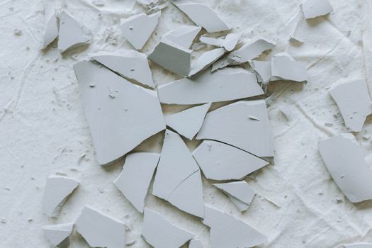 Broken ceramic tiles scattered on a textured white surface, creating an abstract composition.