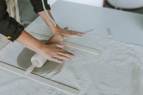 Free Hands rolling clay for pottery on a workbench with a rolling pin. Stock Photo