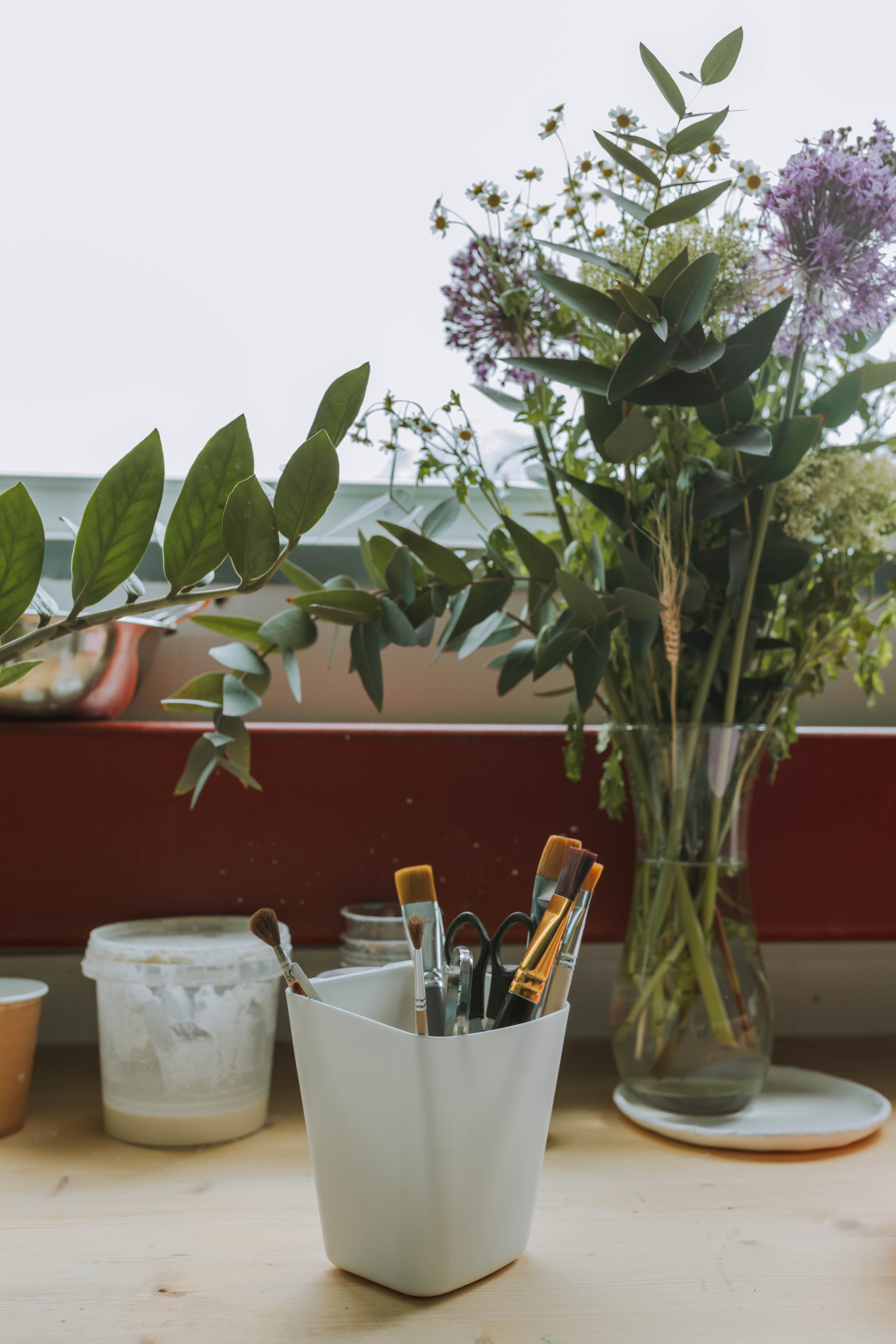 A creative workspace with brushes and a vase of fresh flowers adds inspiration.