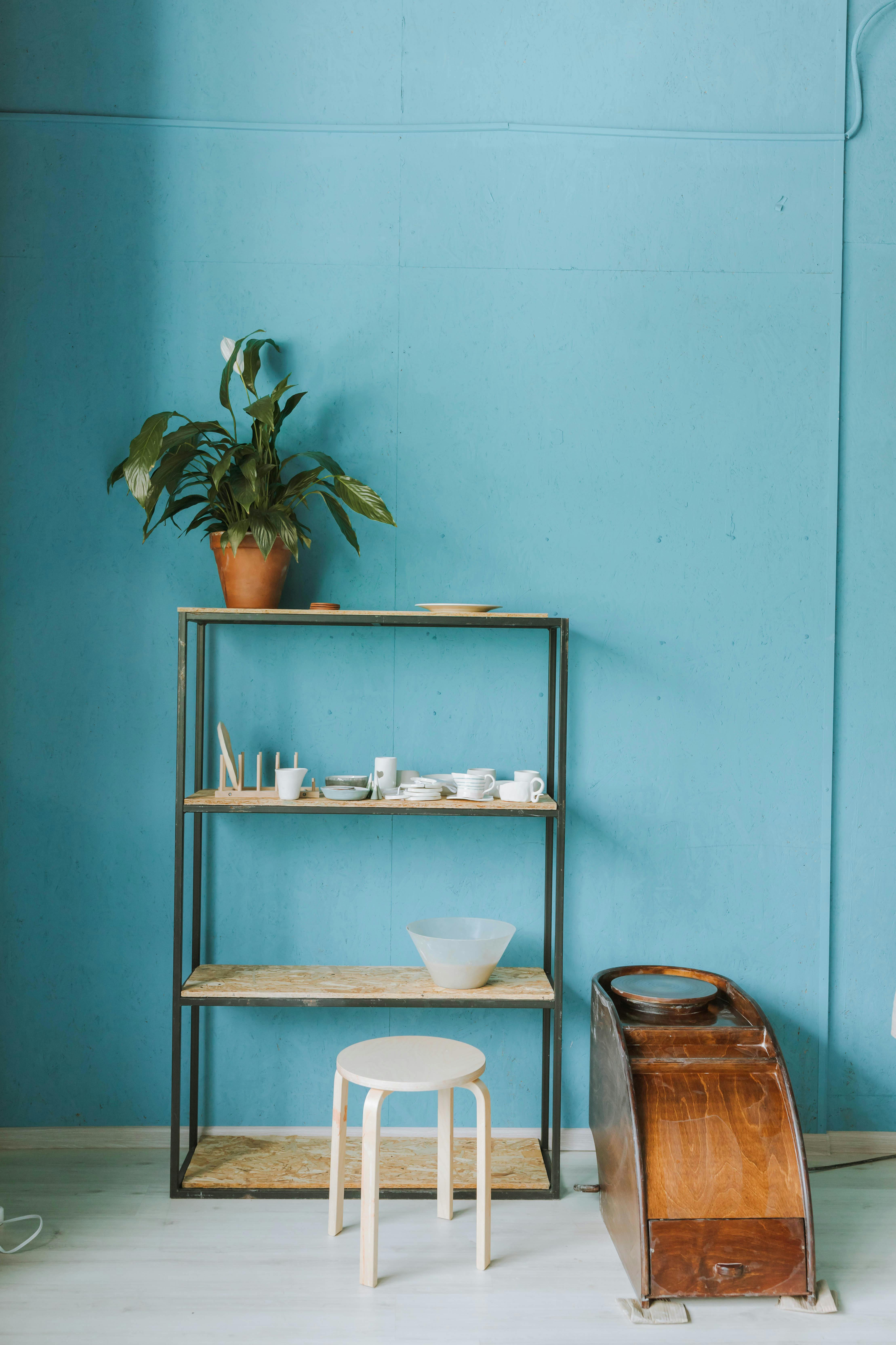 Free A clean and minimalistic pottery workshop featuring a shelf with ceramics and a wooden chair against a blue wall. Stock Photo