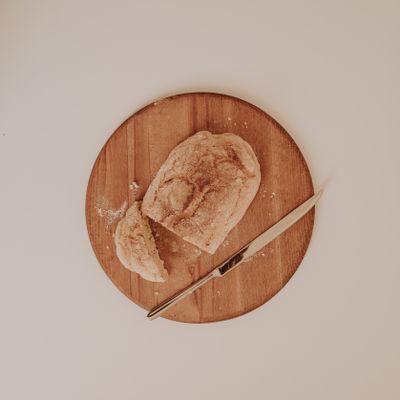 Rustic loaf part-sliced on a round wooden board, photo by Sarah on Pexels