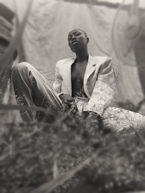 Free From below of black and white confident bald young ethnic lady in fashionable blazer on naked body sitting on chair with legs spread and looking at camera Stock Photo