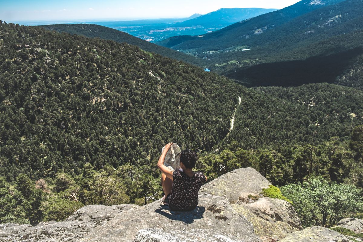 A traveller seated on a rock, reading a map at the top of a hill.