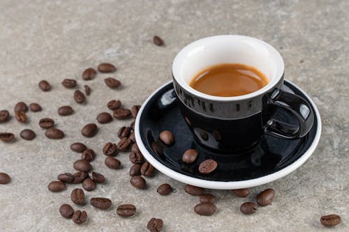 Free Coffee in Black Ceramic Cup and Saucer with Scattered Beans Stock Photo