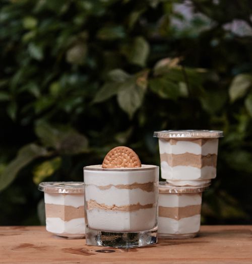Free Delicious layered dessert cups topped with biscuits, set on a rustic wooden table with leaves in the background. Stock Photo
