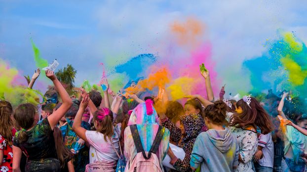 Crowds celebrating Holi with colorful powder under a bright sky.