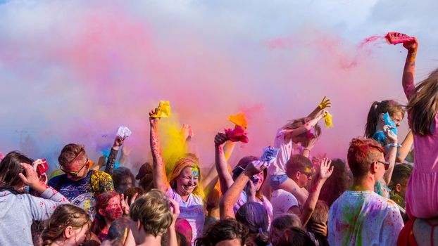 People enjoying a colorful festival, throwing vibrant powder in the air under a sunny sky.