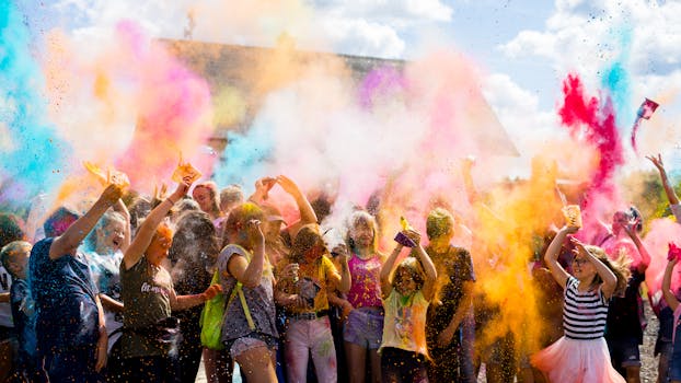 A lively outdoor festival with a crowd enjoying vibrant colored powders under the daylight.