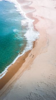 A breathtaking aerial view of waves crashing on a sandy beach with people walking along the shore.