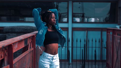 Free Black woman in a denim jacket and crop top on a balcony, gazing afar. Stock Photo