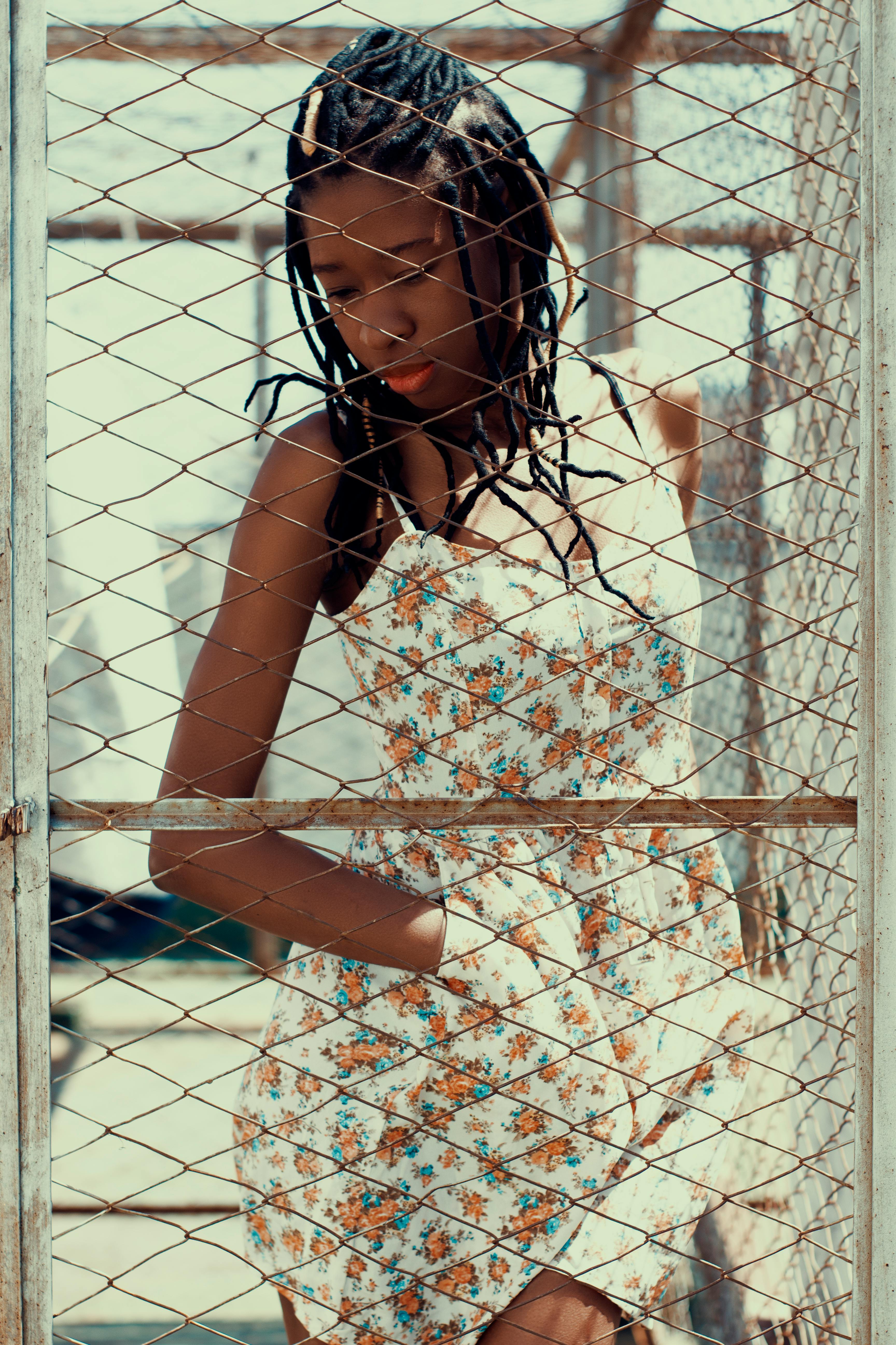 woman in floral dress standing behind metal chain link fence