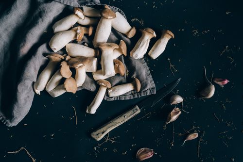 Free Fresh king oyster mushrooms on a dark surface with a knife and garlic, ready for cooking. Stock Photo