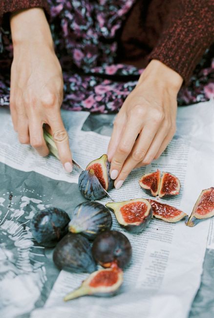A person slicing fresh figs on newspaper, featuring a rustic and natural presentation.
