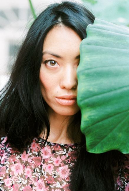 A woman's face partially covered by a large green leaf, creating a natural and mysterious portrait.