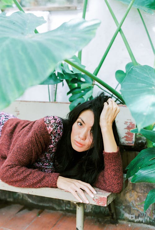 Photo of a Woman Lying on a Bench Near Green Plants