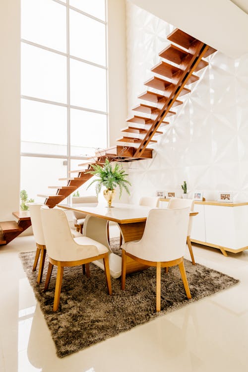 Free Minimalistic design of spacious room with second level space and wooden staircase against large windows in modern house in daytime Stock Photo