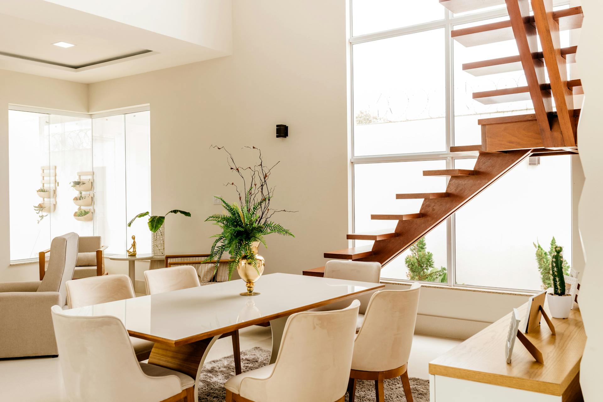 Interior of light living room with wooden stairs and table with comfortable chairs in contemporary house