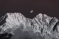月光下，白雪皑皑的山峰呈现出单色景色，云层环绕